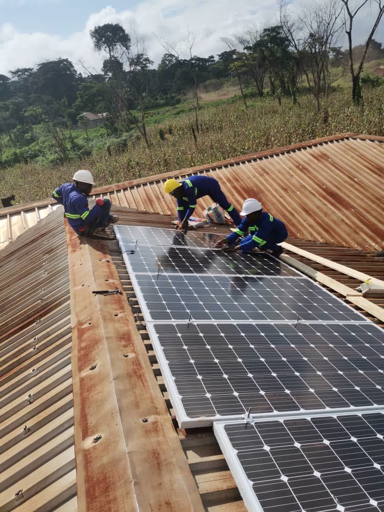 Technicians mounting solar panels on a health facility roof
